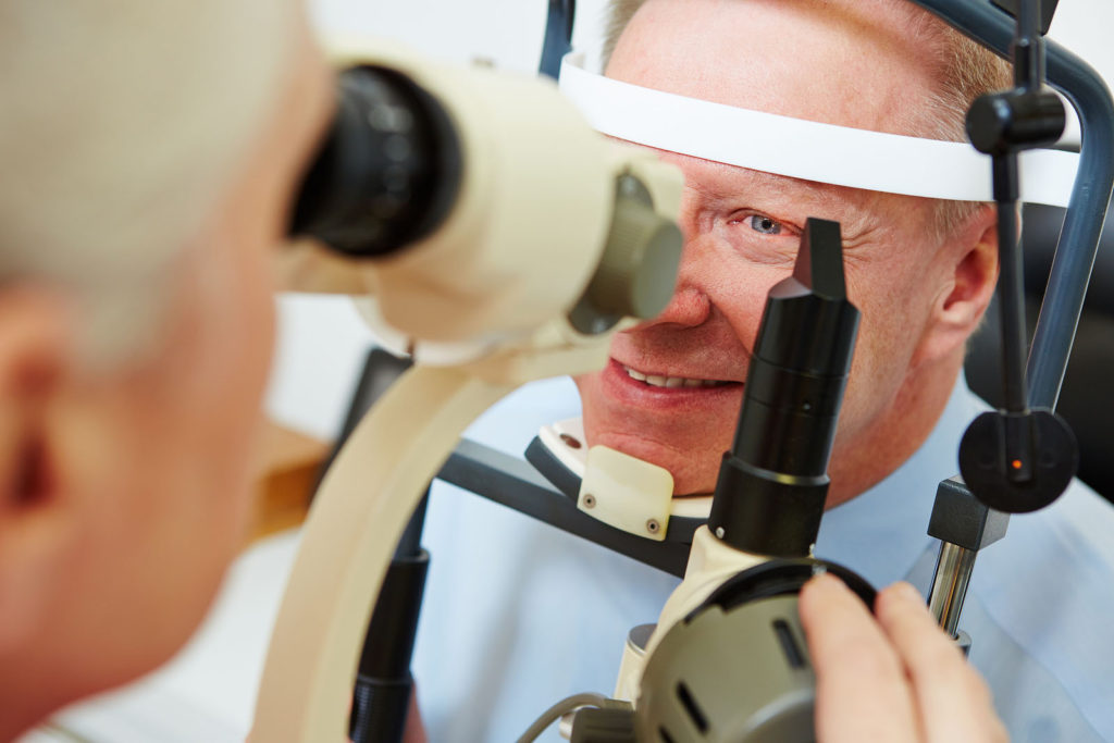 Senior man at optician looking in slit lamp to get his cornea ex