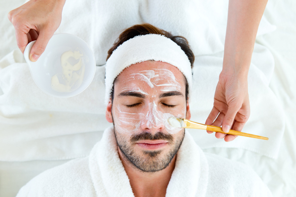 Portrait of man with clay facial mask in beauty spa.