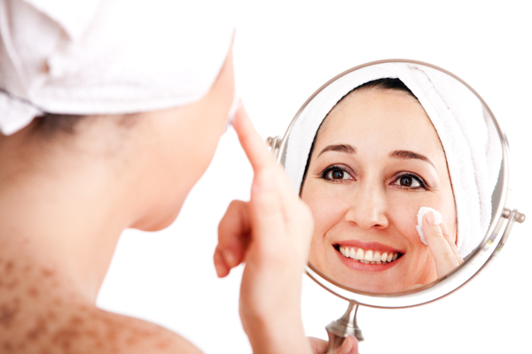 Beautiful happy smiling woman face applying exfoliating cream as anti-aging skincare treatment while looking at mirror, isolated.