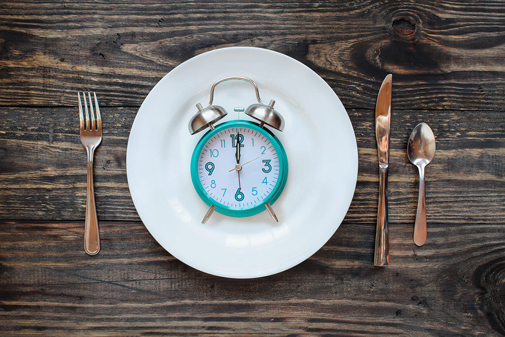 Twelve hour intermittent fasting time concept with clock on plate over a rustic wooden table / background. Top view.