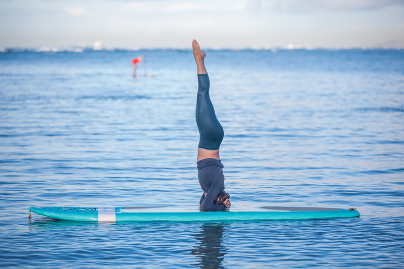 Sunny morning work out a pretty young woman in SUP Yoga practice head stand at Ala Moana Hawaii